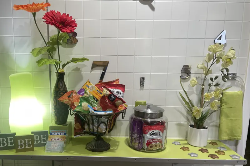 A shelf with snacks, flowers, a soft glowing lamp and small cards with kind words.